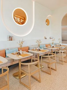 the interior of a restaurant with white walls and wooden tables, beige chairs, and gold accents