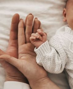 a person holding a baby's hand while laying on top of a white blanket