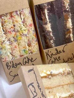 three boxes filled with different types of cakes on display in front of other boxes that have writing on them