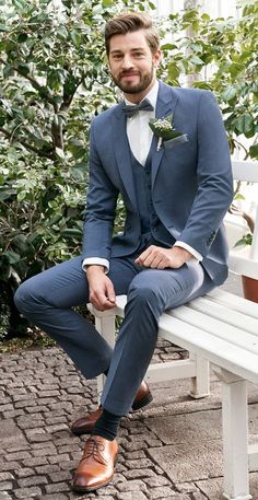 a man in a blue suit sitting on a white bench wearing brown shoes and a bow tie