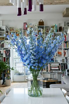 a vase filled with blue flowers sitting on top of a white table in front of a bookshelf