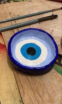 a blue and white bowl with an eyeball painted on the side next to paintbrushes