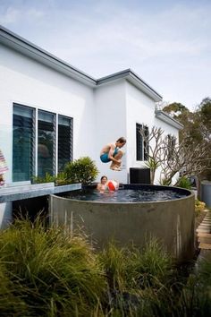 a man jumping into an outdoor hot tub in front of a house with two children