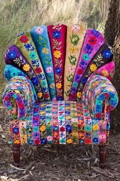 an upholstered chair with colorful fabrics on it's back and arm rests in front of a tree