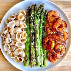 a white plate topped with pasta, shrimp and asparagus next to broccoli