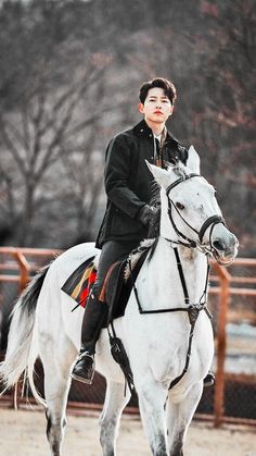 a young man riding on the back of a white horse in an enclosed area with trees