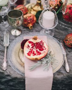 the table is set with silverware and pomegranates