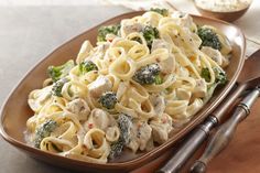 a pasta dish with broccoli and chicken is on a brown serving platter