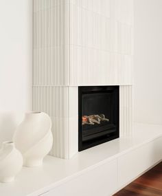 a white fireplace with two vases on top of it and a fire place in the middle