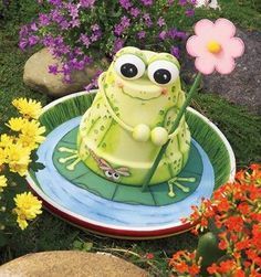 a green frog cake sitting on top of a plate with flowers in the back ground
