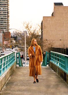 a woman in a fur coat walking across a bridge
