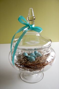 a clear glass container with blue eggs in it and a bow on the top, sitting on a table