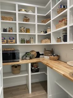 an organized pantry with white shelving and wooden counter top, baskets on the shelves