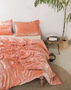a bed with an orange comforter on top of it next to a potted plant