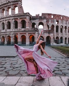 a woman is dancing in front of the colossion with her dress blowing in the wind