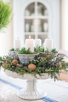 a table topped with a white vase filled with lots of greenery and lit candles