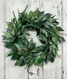 a green wreath is hanging on a white wooden door with leaves and berries around it