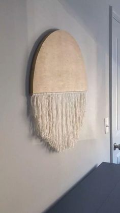 a white wall hanging on the side of a room with a wooden circle and tassels