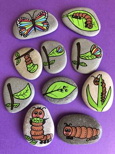 rocks with pictures of bugs, caterpillars and leaves painted on them sitting on a purple surface