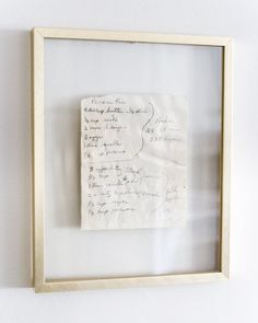 a piece of paper with writing on it in a wooden frame against a white wall