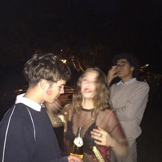 three young people standing next to each other at night with one holding a wine bottle