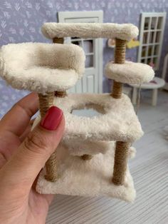 a hand holding a cat tree in front of a doll house with furniture and accessories