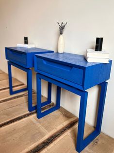 two blue side tables with vases on each one and books sitting on the other