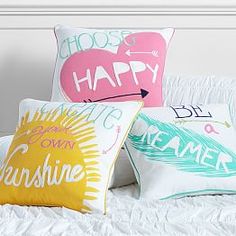 three pillows with different sayings on them sitting on a white bed in a room