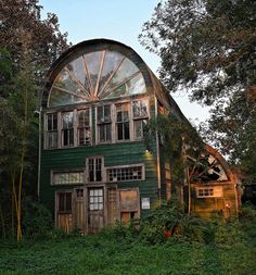 an old green barn sits in the middle of some trees and has a large round window