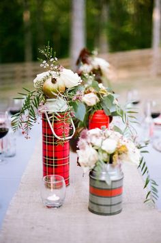 the table is set with red and white vases filled with flowers, greenery and apples