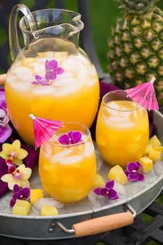 two glasses filled with orange juice next to a pitcher and pineapples on a table