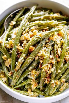 a white bowl filled with green beans covered in crumbled breadcrumbs