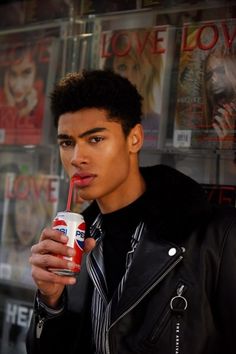 a young man holding a drink in his hand and looking at the camera while wearing a leather jacket