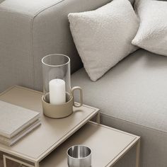 a coffee table with two cups and a candle on it next to a gray couch