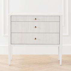 a white chest of drawers with two gold handles on each drawer, against a white wall