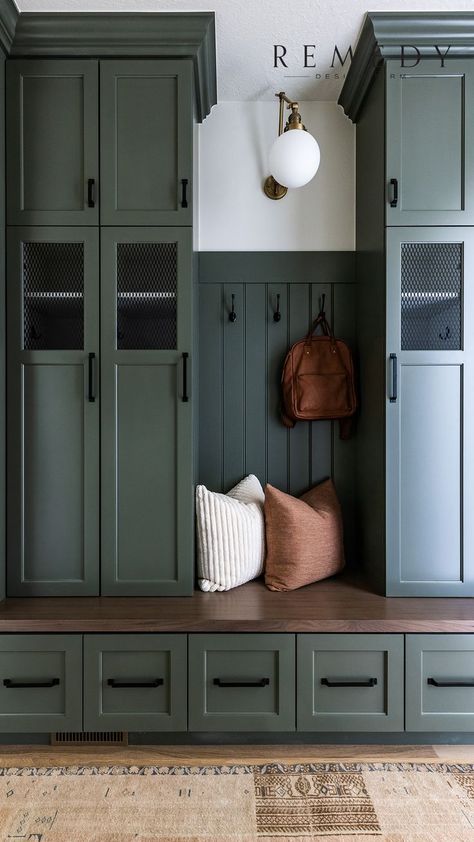 a dark colored, moody mudroom with a dark green olive tone paint. the mudroom features tall lockers for organization and storage with black handles and hardware. There are hooks on the textured wall to hang backpacks and keys. There are two pillows on the bench seat that are a white pillow and tan pillow. There is a white spherical orb light with gold details. There are drawers and cupboards and cabinets and hardwood floors with a tan rug a vintage rug. A great display of interior design Design, Interior, Vintage, Style, Gang, Dekorasyon, Hol, Haus, Case