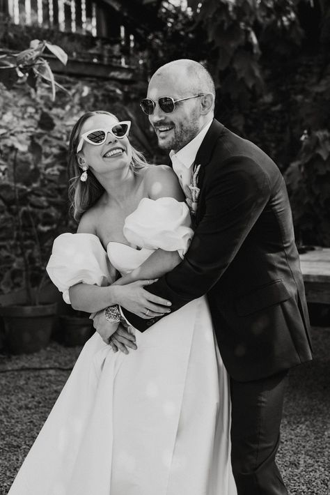 Groom wearing sunglasses hugs the bride from behind in a puff sleeve wedding dress with white sunglasses Bride White Sunglasses, Wedding Pictures With Sunglasses, Couple Sunglasses Photo Ideas, Bridal Party With Sunglasses, Wedding Day Sunglasses, Sunglasses With Wedding Dress, Bride And Groom Sunglasses Photo Ideas, Bride With Sunglasses Photo Ideas, Wedding Dress Sunglasses