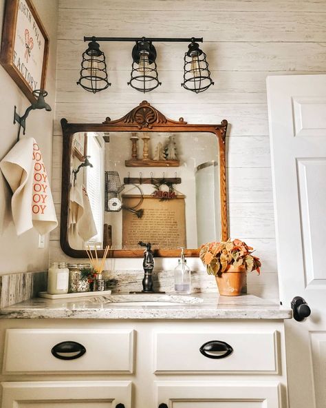 Rustic wood shiplap and a vintage wood-framed mirror decorate the wall in this small bathroom. A black metal light fixture is mounted on the wall above, with rustic bathroom decor hung on the adjacent wall. Lugares, Decor Inspiration, Salle De Bain, Timeless Bathroom, Vintage Bathroom, Modern Farmhouse Bathroom, Ship Lap Walls, Bathroom Inspiration Decor, Bathroom Decor