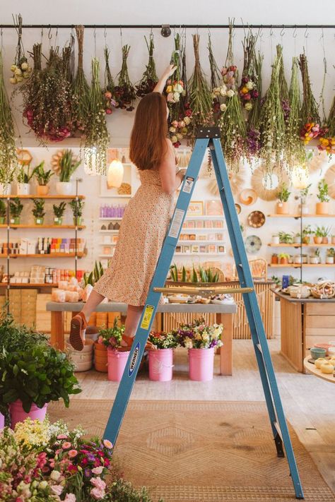 a woman on a ladder in a shop, hanging flowers upside down to dry them out Floral, Flower Shop Decor, Flower Shop Display, Flower Boutique, Flower Market, Floral Shops, Flower Shop Design, Flower Studio, Flower Cafe