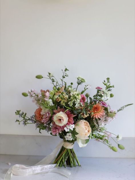 Peach toned bridal bouquet with trailing ribbons sitting on a marble block. Floral, Wildflower Wedding Bouquet Summer, Garden Rose Bouquet Wedding, Spring Wedding Flowers, Wildflower Wedding Bouquet, Wildflower Wedding Bouquets, Spring Wedding Bouquet, Garden Rose Bouquet, Spring Wedding Bouquets