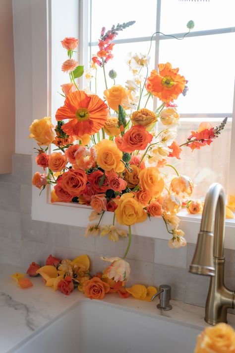 a gold and orange floral installation by WildFlora in Los Angeles in a pink kitchen with a white sink. flowers spill out of the sink and bloom in the window sill. Hochzeit, Boda, Mariage, Flores, Tulip Wedding, Orange, Bouquet, Ranunculus Wedding, Orange Wedding