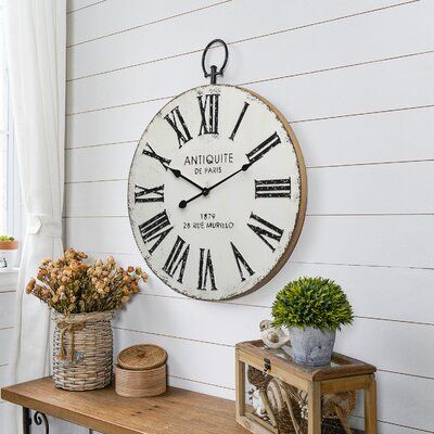 Add style to your decor and keep track of your hours with our Round Metal Wall Clock with Top Loop. The Metal Wall Clock features a distressed white painted metal, an embossed body with rustic black Roman numeral markings and arms, a distressed black rim, a light brown wood frame, and an industrial metal accent at the top, Refresh and revive your space! Perfect accent decor for a kitchen, dining room, bedroom, library, coffee house, or office. Battery required, not included. | Gracie Oaks Jamel Metal, Retro, Metal Wall Clock, Decorative Pillows, Metal Walls, Wall Clock, Unique Clocks, Wall, Distressed Painting