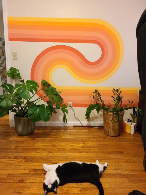 70s wavy wall art with pink peach yellow orange tones in a rainbow looping together with a big monstera plant and zz plant on the right wooden floor with a very cute black and white Cat laying on the floor looking at the camera Design, Vintage, Retro, Colorful Retro Bedroom, Groovy Room Decor, Groovy Room, Groovy Bedroom, 70s Stripe Wall, Groovy Interiors