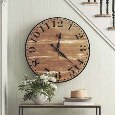 This circular wooden clock adds a vintage-inspired feel to your modern farmhouse or industrial-styled space. Made in the USA from solid cedar in a distressed stained finish, this analog clock features black arabic numerals over a chestnut-colored base and antique-style spade hands. The numbers are surrounded by small black dots at the five-minute mark and larger black dots at the hour mark, with a single black ring outlining the entire piece. It takes one AA battery (sold separately) and uses a Home Décor, Modern Farmhouse, Boho, Mantle Decor, Large Wooden Wall Clock, Farmhouse Wall Clock, Farmhouse Wall Clocks, Wood Wall Clock, Wall Clock Decor Living Room