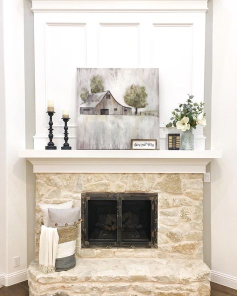 Tan, white and gray woven basket is placed on the hearth of a beige painted stone fireplace. Gray artwork is perched on the ivory fireplace mantel in front of white decorative molding. Art, Farmhouse Style, Diy, Farmhouse, Ideas, Farmhouse Charm, Above Fireplace Ideas, Fireplace Facing, White Fireplace Mantels