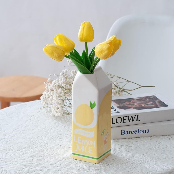 yellow tulips in a white vase on a table next to books and magazines