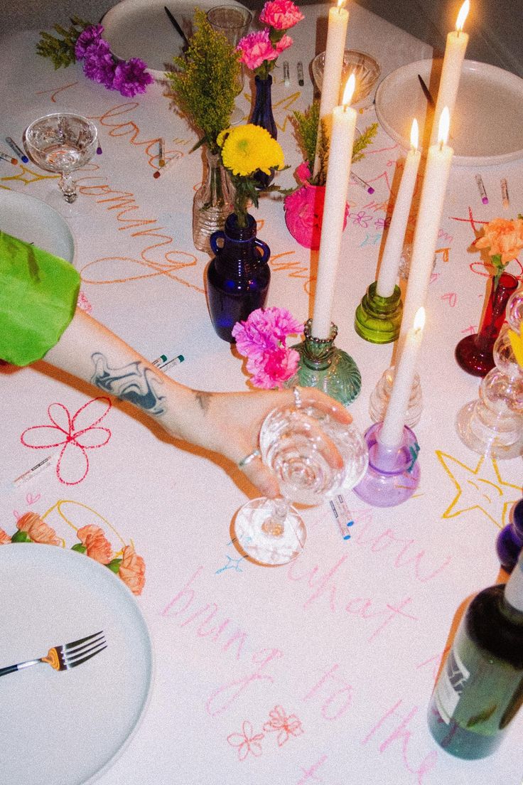 a table topped with lots of candles and plates covered in writing next to wine glasses