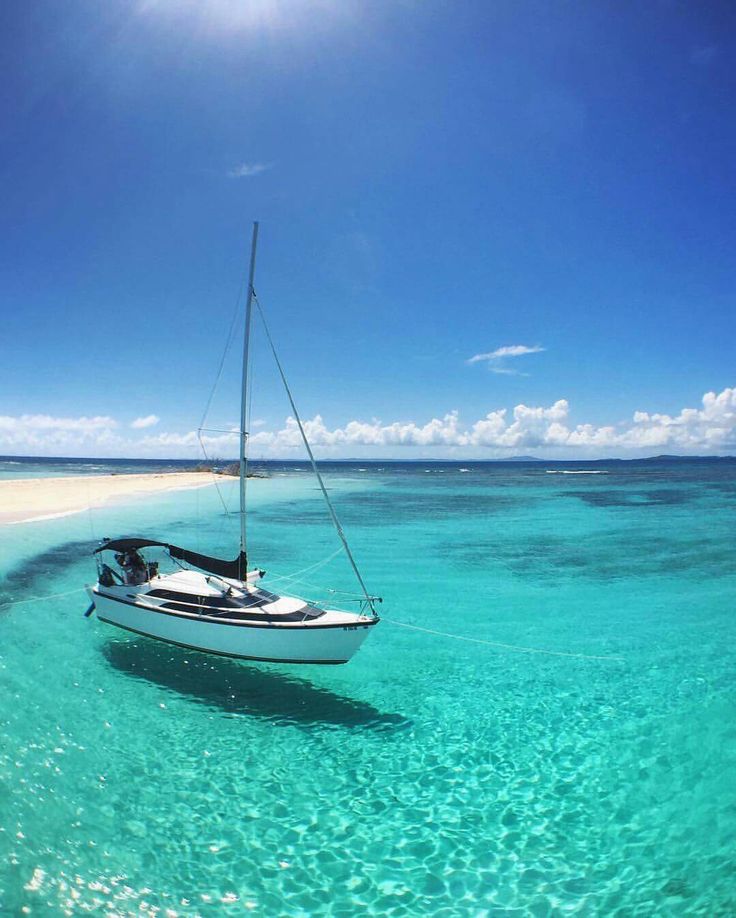 a sailboat floating in the clear blue water on an island with white sand beach