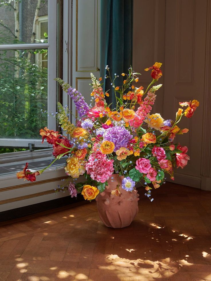 a vase filled with lots of colorful flowers sitting on top of a wooden floor next to a window