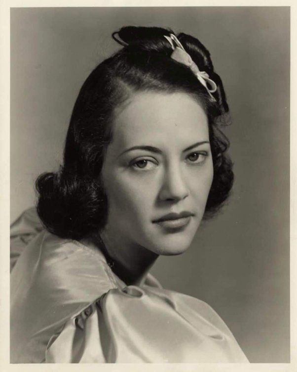 an old black and white photo of a woman with a bow in her hair wearing a blouse